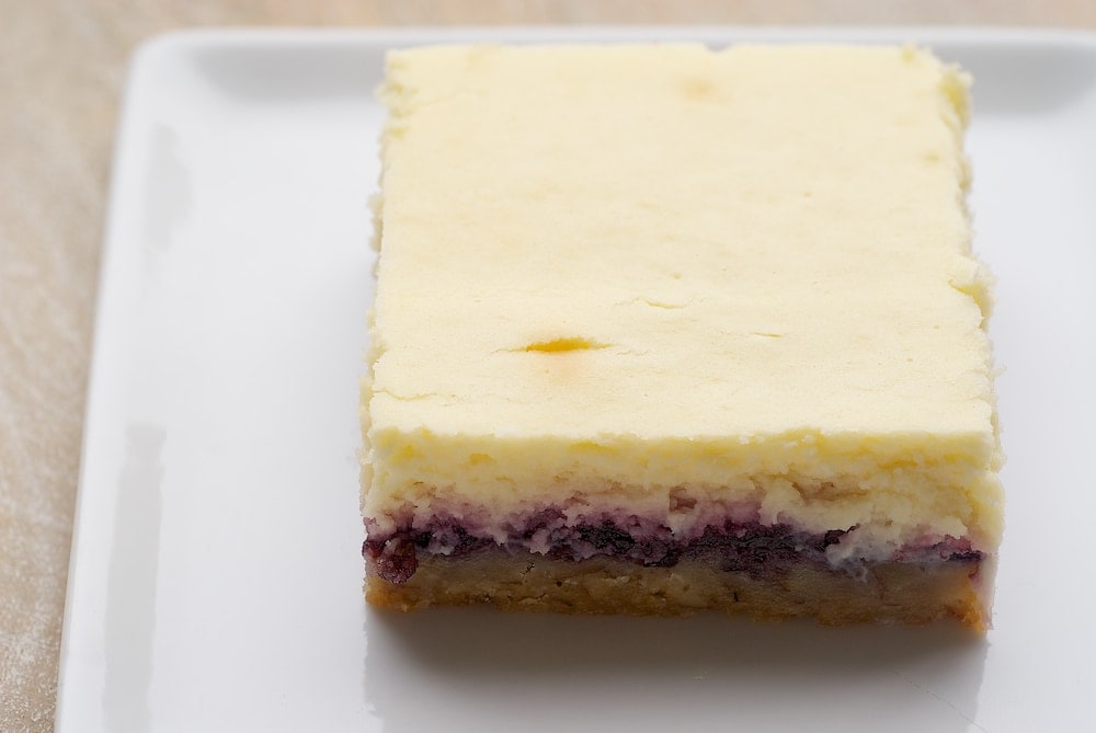 Lemon Blueberry Cheesecake Bars combine a nutty crust, blueberry preserves, and a lemony cheesecake for an irresistible dessert. - Bake or Break